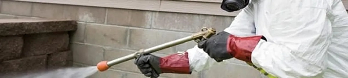 Pest control technician applying exterior insect treatment along a home foundation in Portland, OR