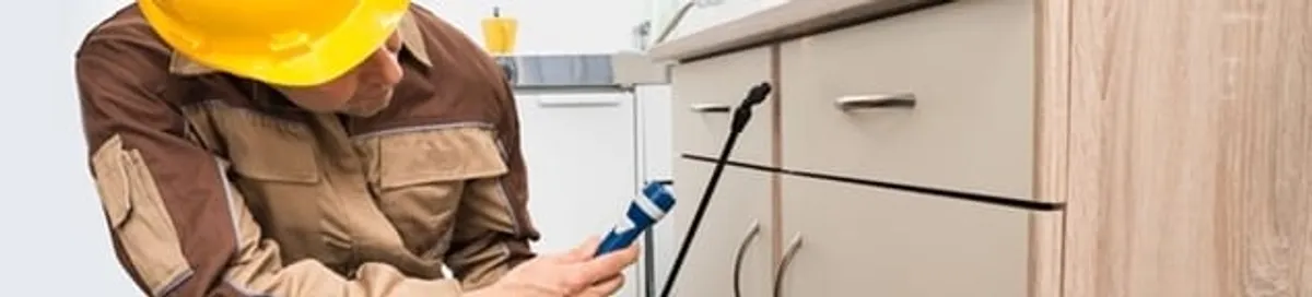 Roach exterminator applying treatment under kitchen cabinets in Portland, OR