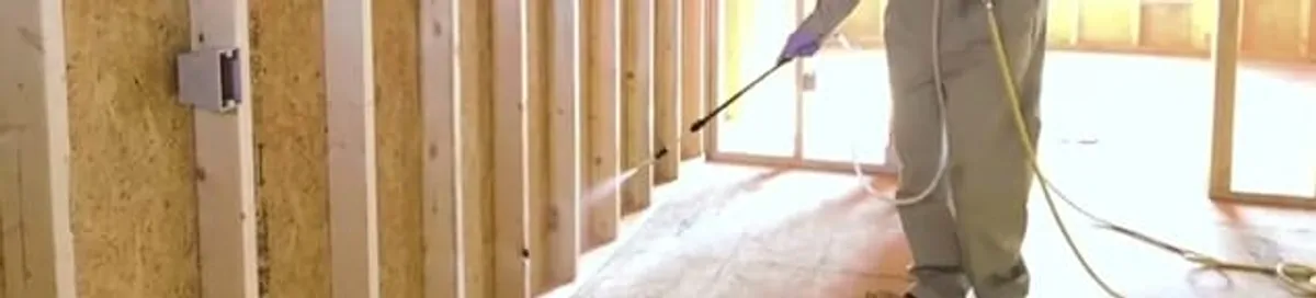 Termite treatment technician applying spray along framing and unfinished walls in Portland, OR