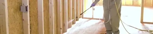 Termite treatment technician applying spray along framing and unfinished walls in Portland, OR